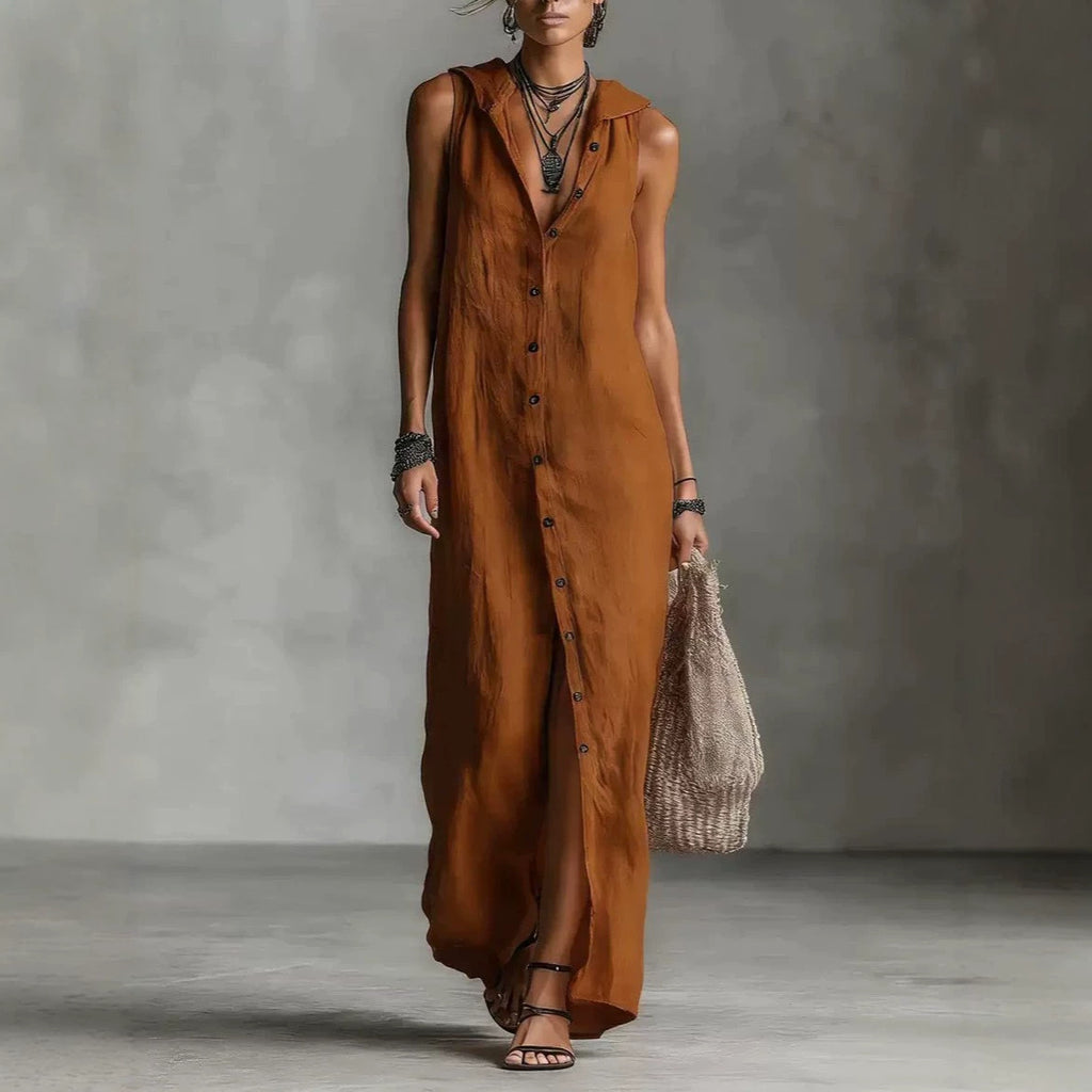 Woman wearing a long brown dress holding a woven bag against a gray background