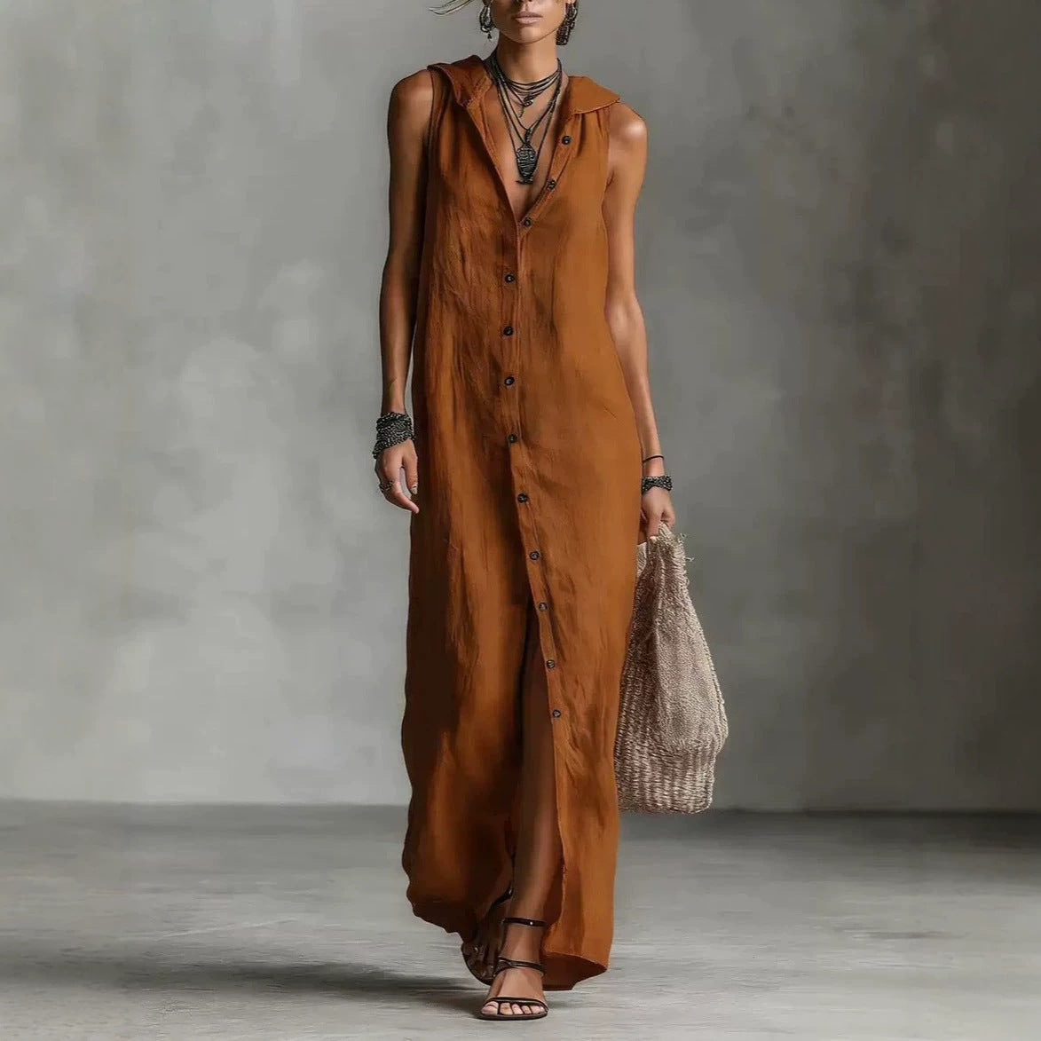 Woman wearing a long brown dress holding a woven bag against a gray background