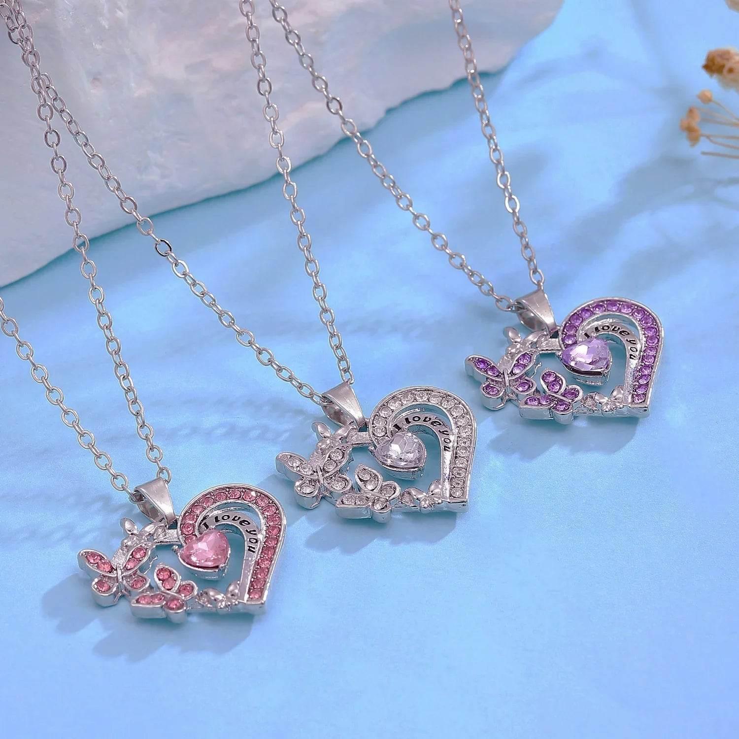 Three silver heart and butterfly pendants with colored crystals on chains, displayed on blue background
