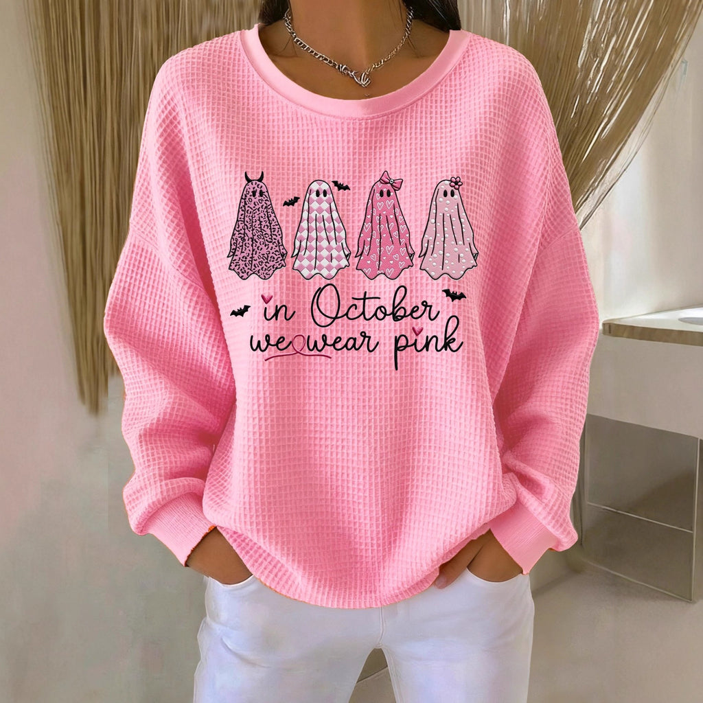 Pink sweatshirt with ghost illustrations and text 'In October we wear pink' worn by a person.