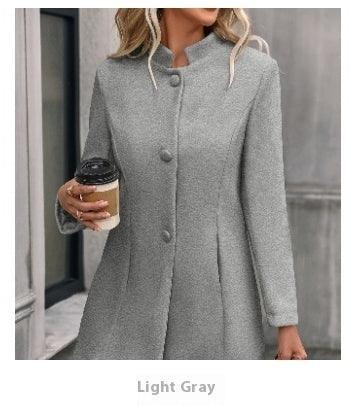 Woman in light gray buttoned coat holding coffee cup, standing outdoors