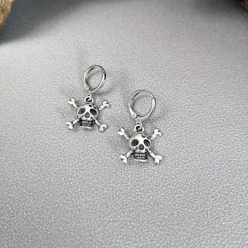 Silver skull and crossbones dangle earrings on textured gray background