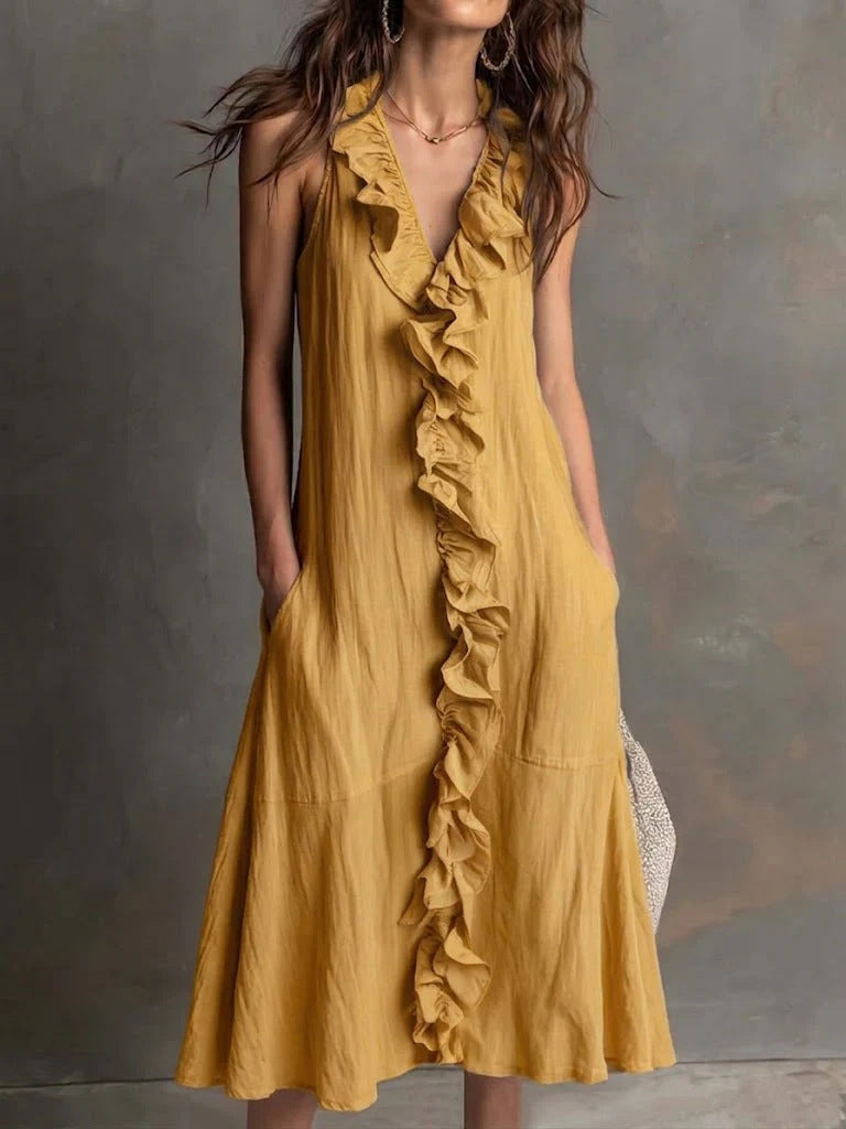 Woman wearing a mustard yellow dress with ruffles against a gray background