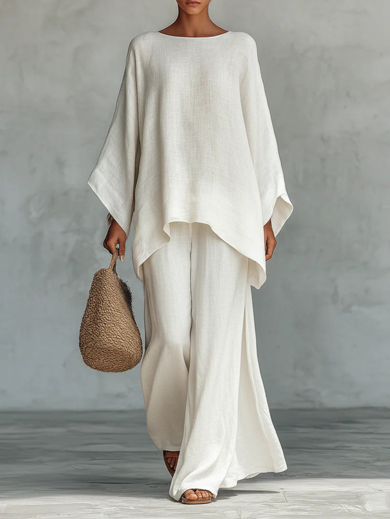 Person wearing a flowing white outfit holding a woven bag against a plain background