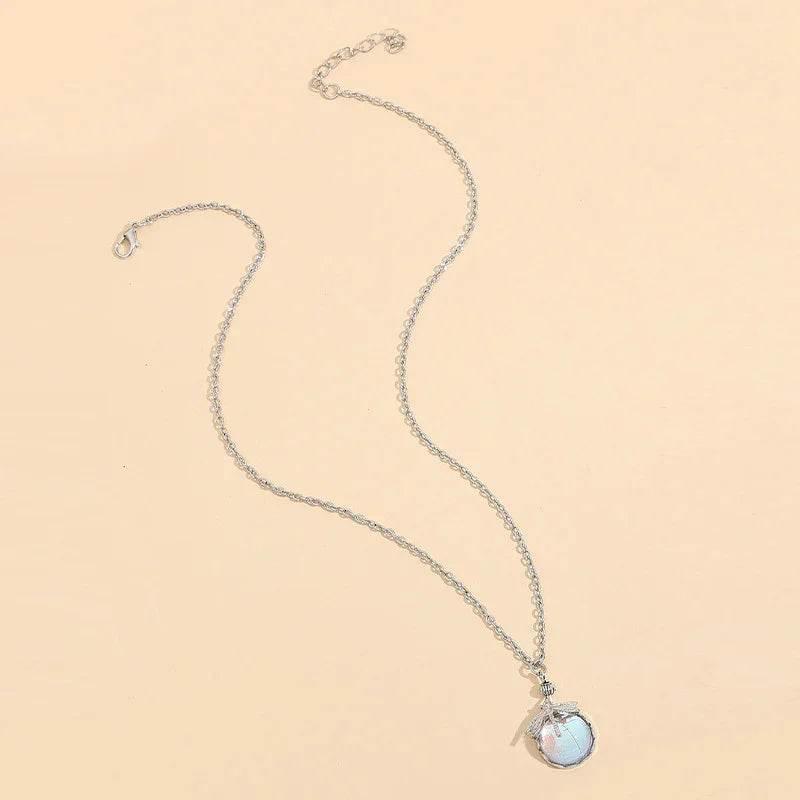 Silver chain necklace with round opalescent pendant and leaf charm on beige background