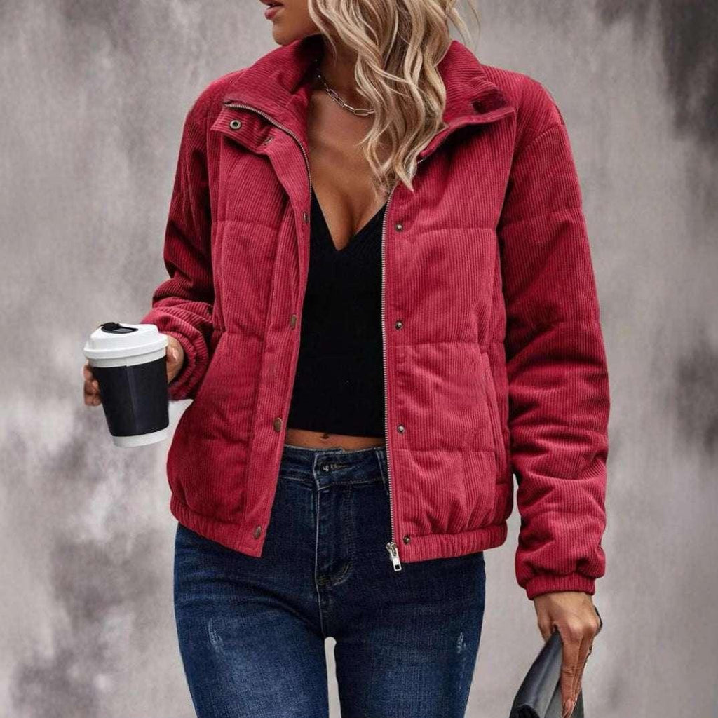 Woman wearing a red corduroy puffer jacket, black top, and blue jeans, holding a coffee cup