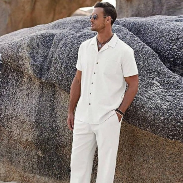 Man in a white outfit standing against a rocky background