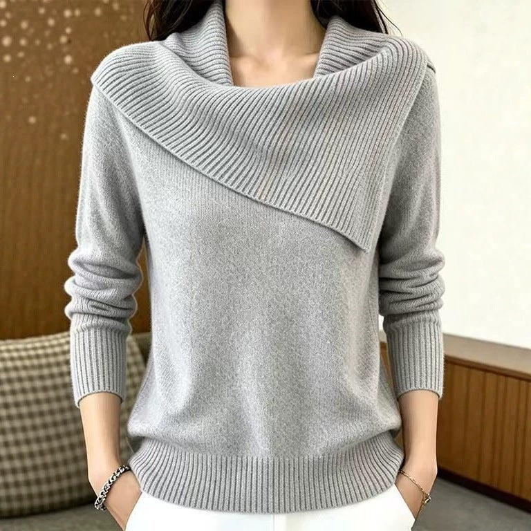 A woman wearing a light gray knit sweater with an asymmetrical draped cowl neckline, long sleeves, and ribbed trim at the collar, cuffs, and hem.