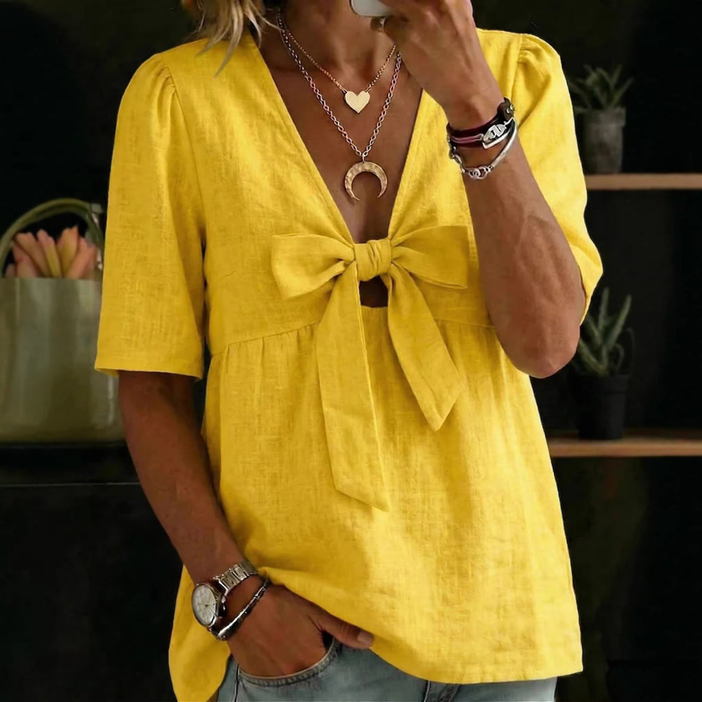 Person wearing a yellow blouse with a bow detail, standing indoors.