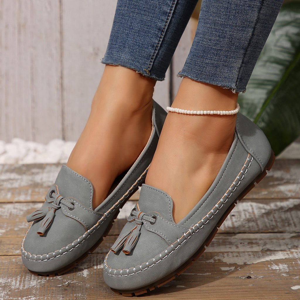 Gray loafers worn with blue jeans on a wooden floor.