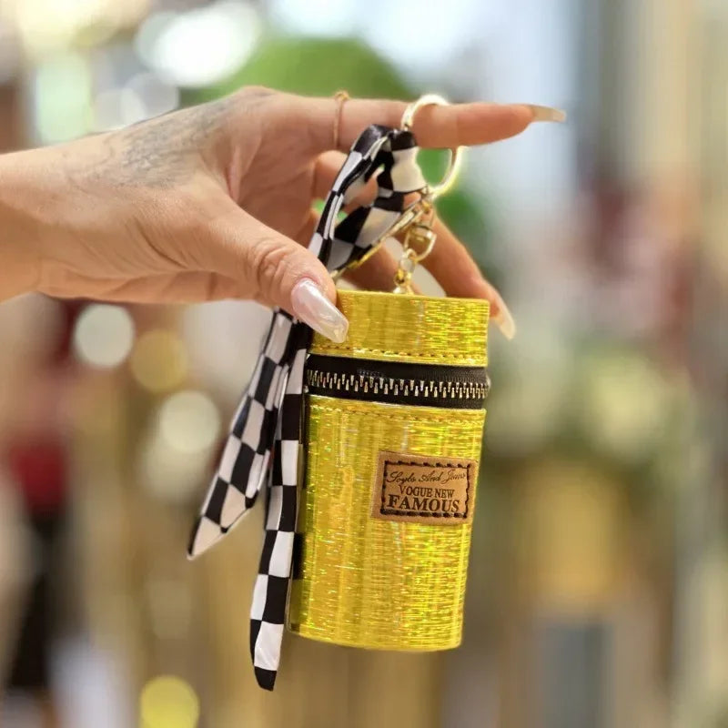 Hand holding a stylish yellow mini bag with zipper, checkered ribbon, and patch detail