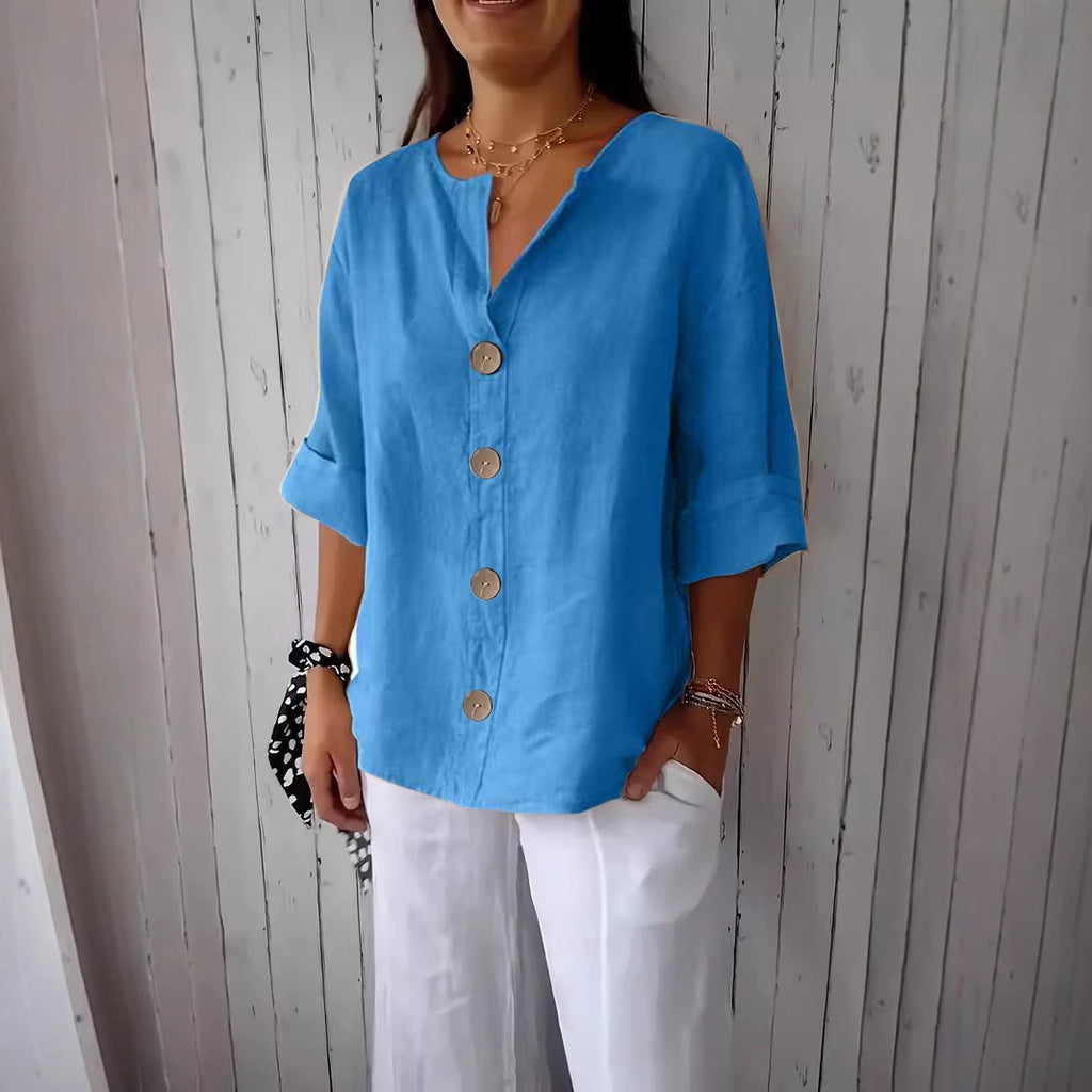Woman wearing a blue button-up shirt and white pants against a wooden paneled wall.