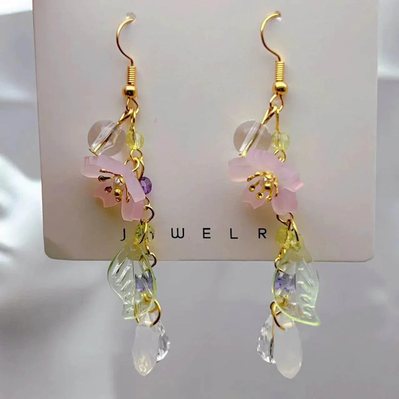Dangling gold earrings with pink flower, crystal beads, and leaf charms on display card
