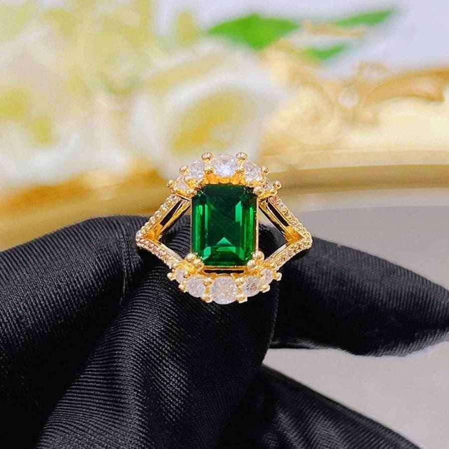 Gold ring with large emerald-cut green gemstone and clear crystal accents, shown on black glove