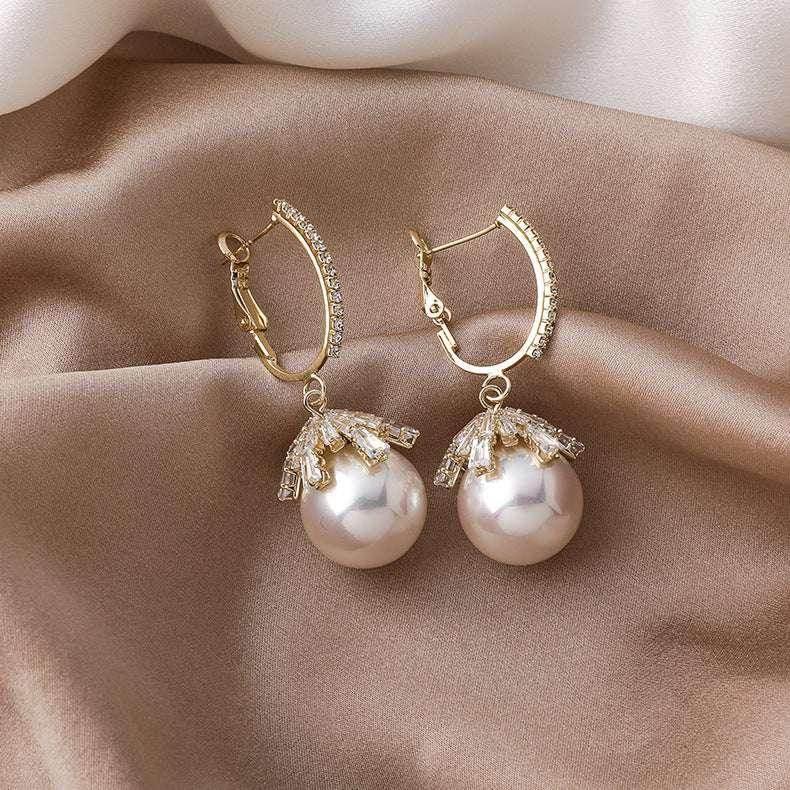 Gold hoop earrings with large pearl drops and crystal accents on satin fabric