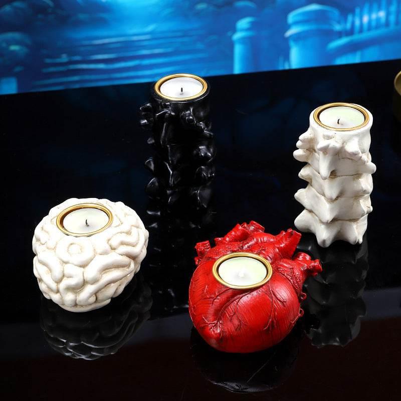 Novelty candle holders shaped like a brain, heart, vertebrae, and black spine, on reflective surface