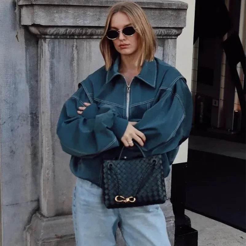Woman in oversized blue denim jacket, sunglasses, and light jeans holding black woven handbag