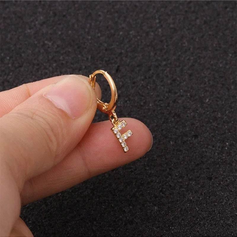 Gold hoop earring with crystal letter F charm held by hand on black textured background