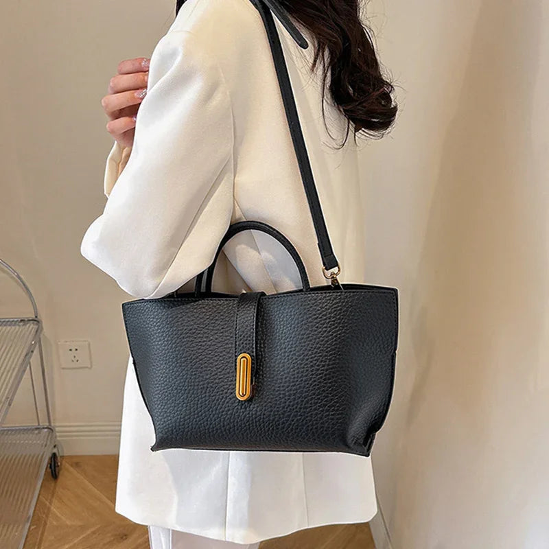 Person holding a black handbag with a gold clasp against a neutral background