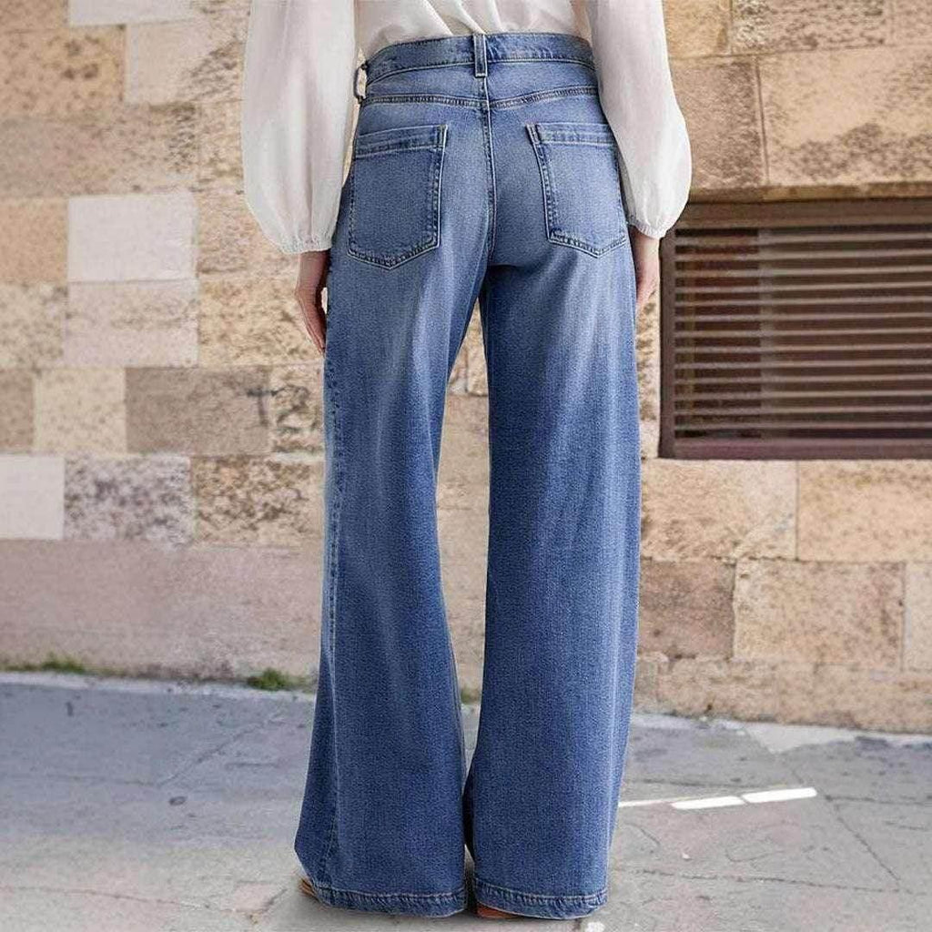 Woman wearing high-waisted wide leg blue jeans and white blouse, standing outdoors