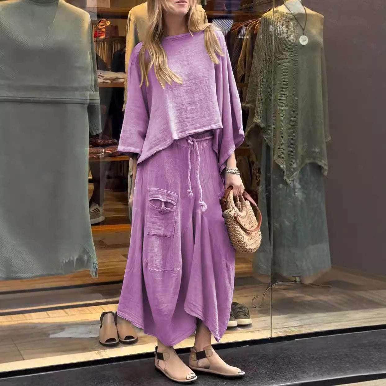 Woman in loose lavender lounge set with drawstring skirt and sandals, holding woven bag, outside clothing store