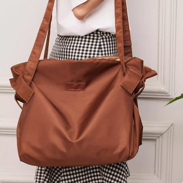 Brown shoulder bag held by a person wearing a checkered skirt against a white wall.