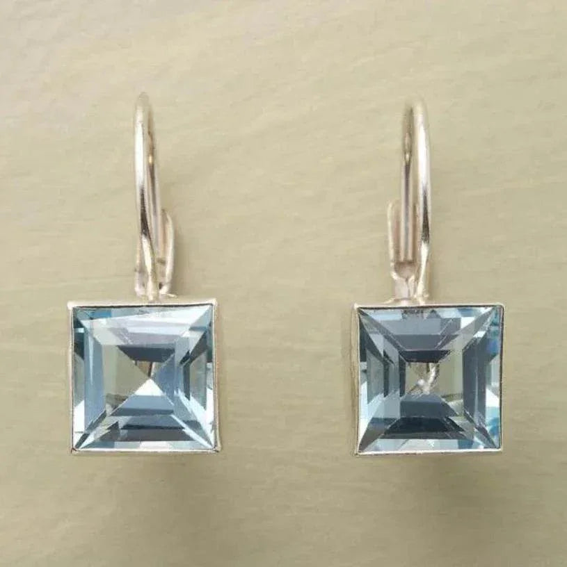 Square cut blue gemstone drop earrings with silver hooks on a neutral background