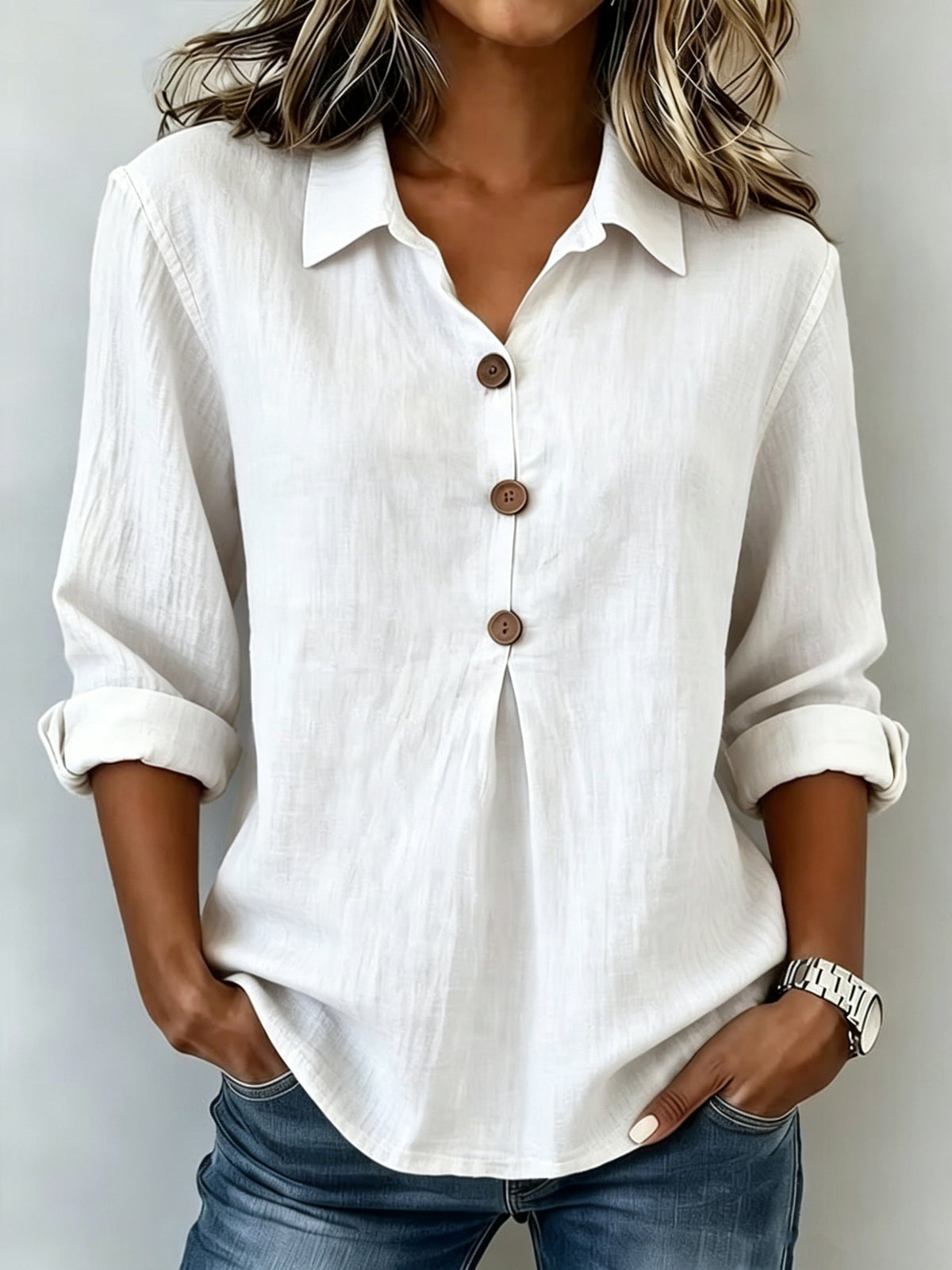 Person wearing a white button-up shirt with rolled-up sleeves and blue jeans on a plain background