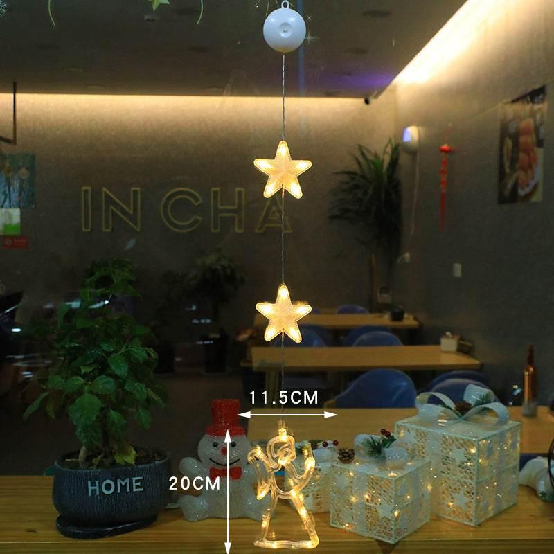 Warm white LED string lights with star and angel shapes hanging in a cozy indoor café setting, featuring decorative holiday gift boxes and festive snowman décor.