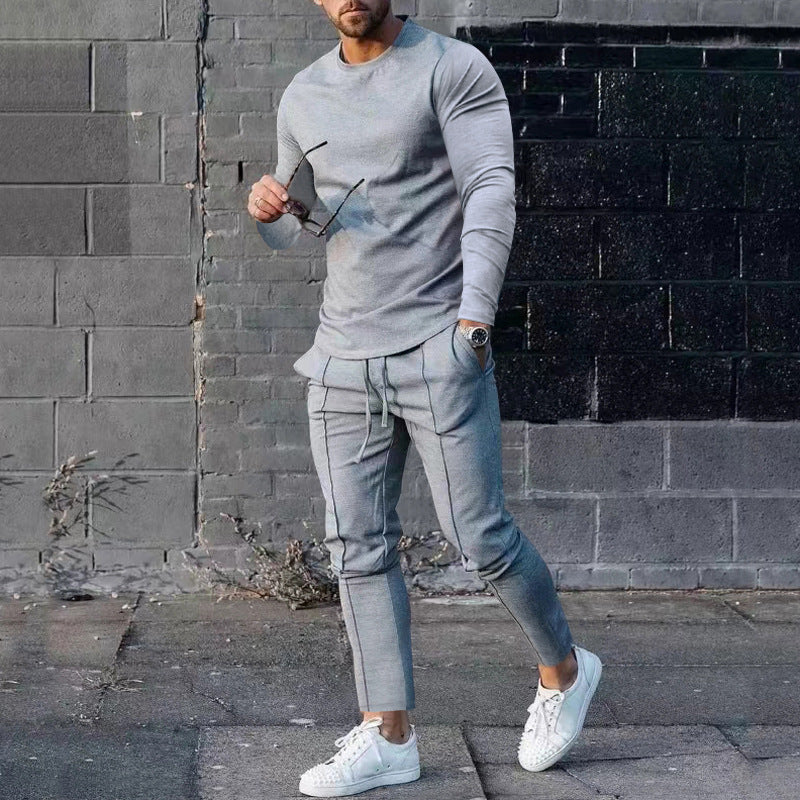 Man wearing a gray tracksuit standing against a brick wall.