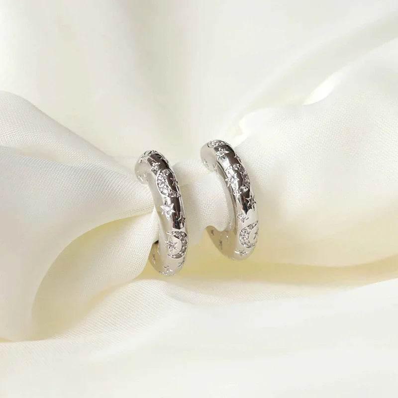Silver hoop earrings with star and moon engravings on white fabric background