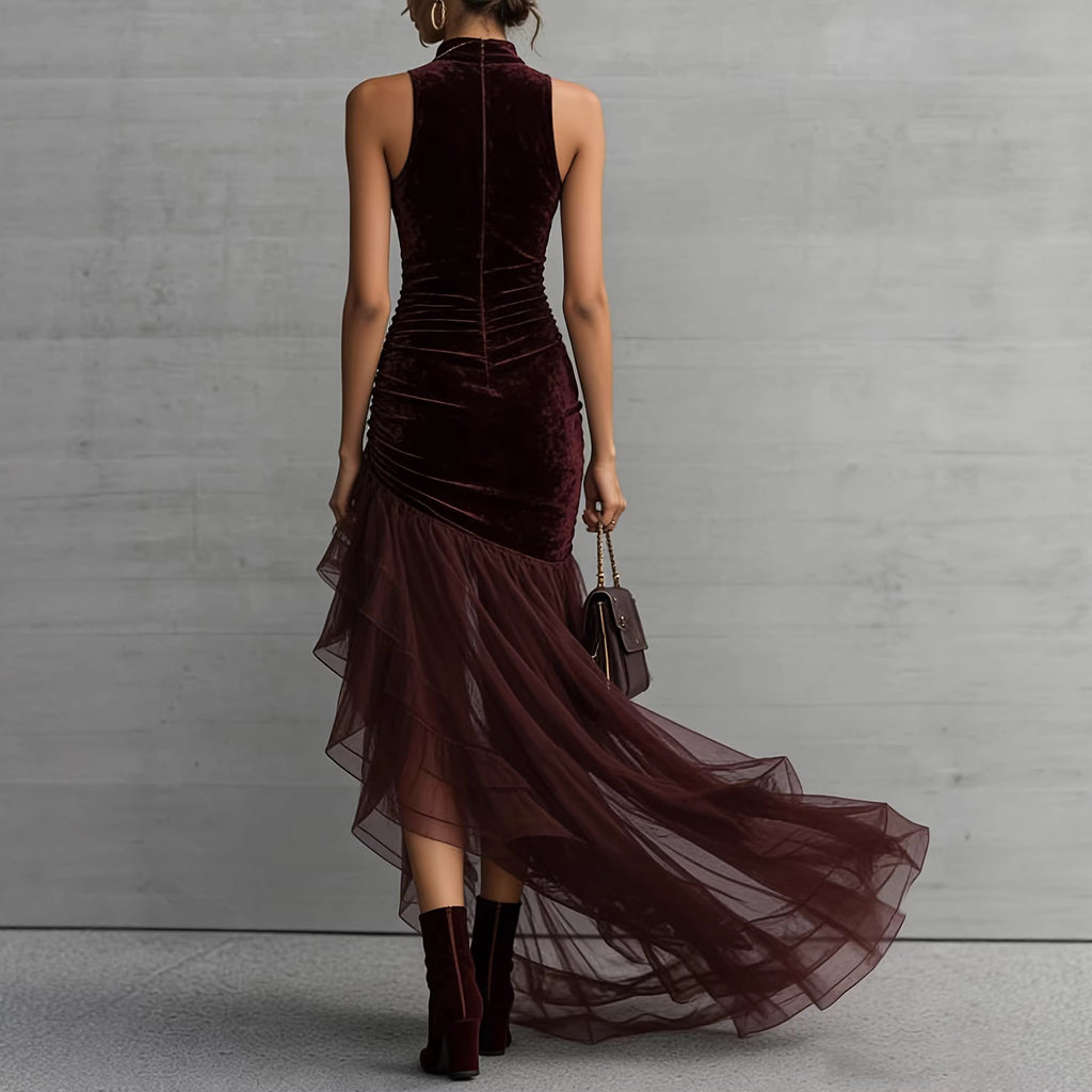 Woman wearing a burgundy velvet dress with sheer overlay against a gray concrete wall.