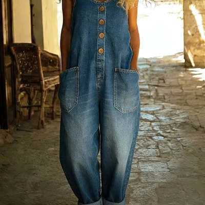 Person wearing a denim jumpsuit in an outdoor setting with stone pavement and wooden chair.