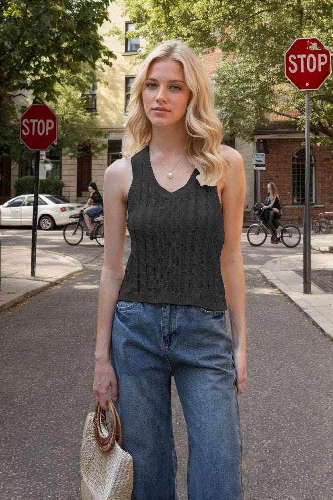 Woman in black knit tank top and wide-leg jeans holding straw bag outdoors on city street