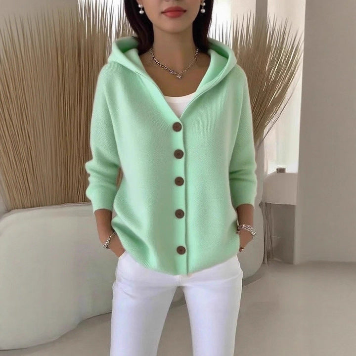 Person wearing a light green cardigan with brown buttons in a minimalistic setting.