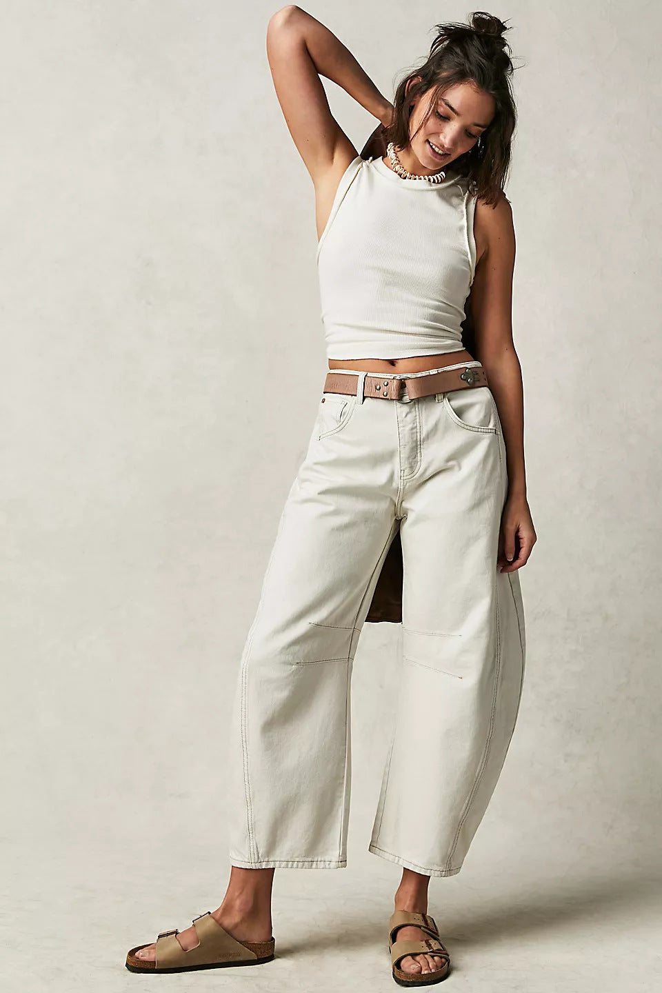 Woman wearing a white sleeveless top and light-colored pants against a plain background