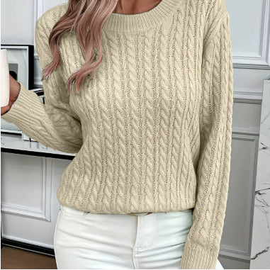 Beige cable knit sweater worn by a person indoors.