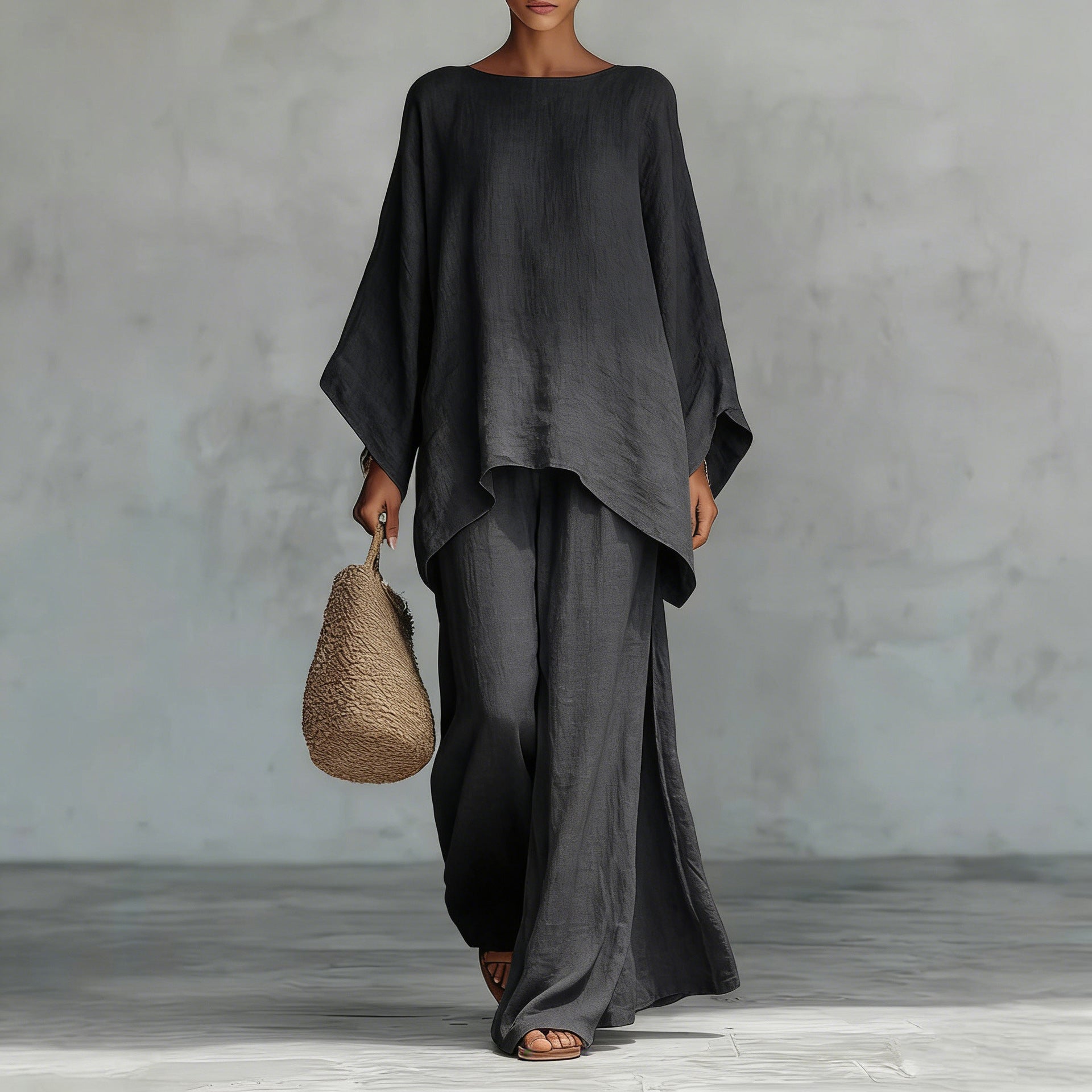 Person wearing a black outfit holding a woven bag against a gray background