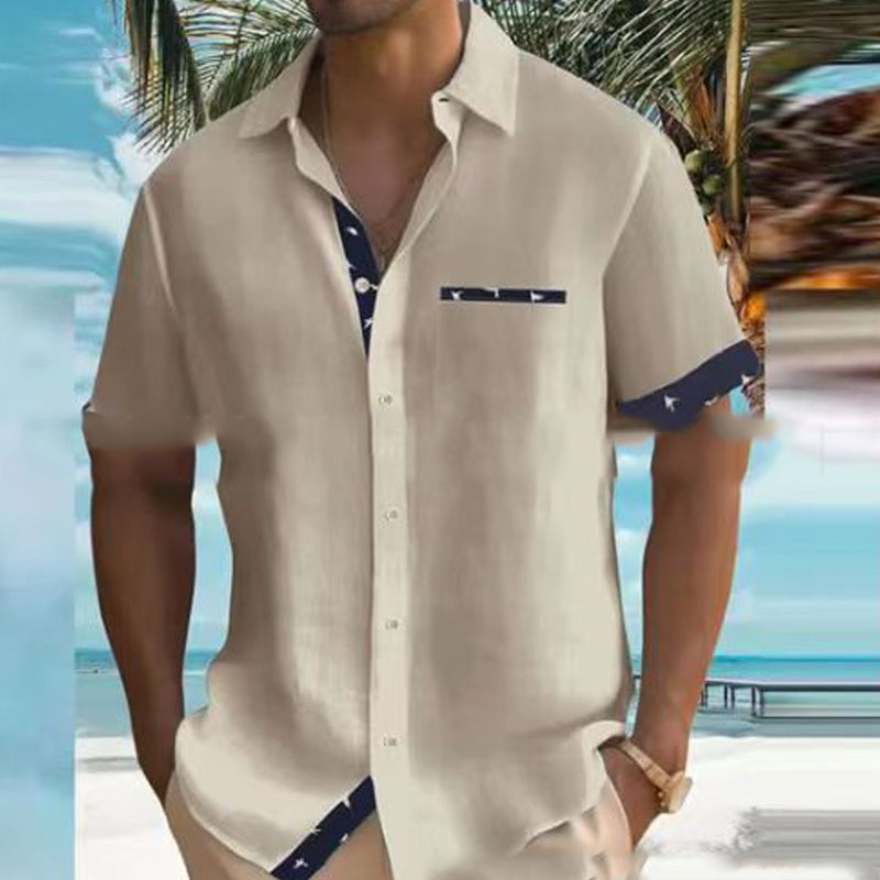 Man wearing a beige short-sleeve shirt with blue accents on a beach.
