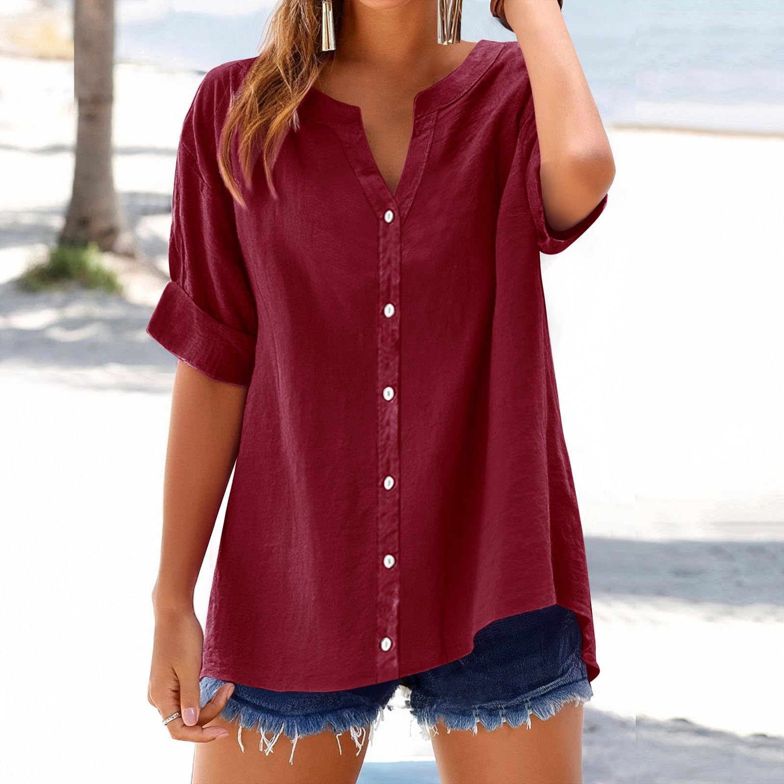 Person wearing a red button-up shirt and denim shorts on a beach.