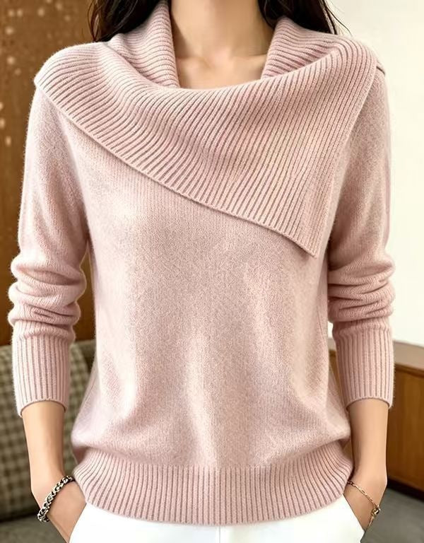 A woman wearing a light pink knit sweater with a wide draped cowl neckline and ribbed trim, paired with white pants.