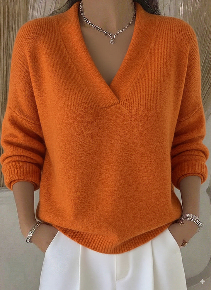 Person wearing an orange sweater and white pants with a neutral background