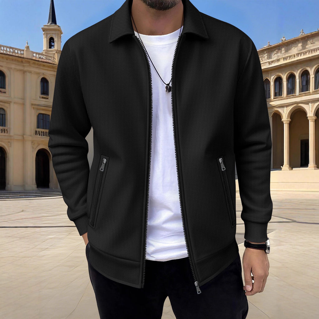 Person wearing a black jacket over a white shirt in front of a historical building.