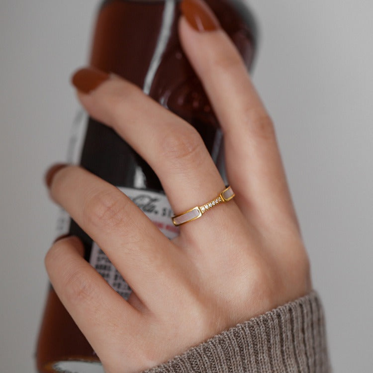 Hand holding a bottle with a gold ring on a neutral background