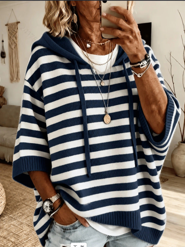 A woman takes a mirror selfie wearing a navy blue and white horizontally striped knit hoodie with wide sleeves, layered over a white t-shirt and paired with light-wash jeans.