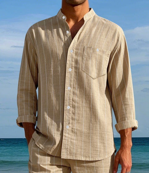 Man wearing a beige striped shirt and pants standing on a beach with blue sky and ocean.