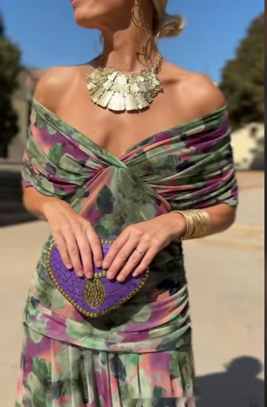 Woman in a colorful dress holding a purple handbag with a gold heart design.