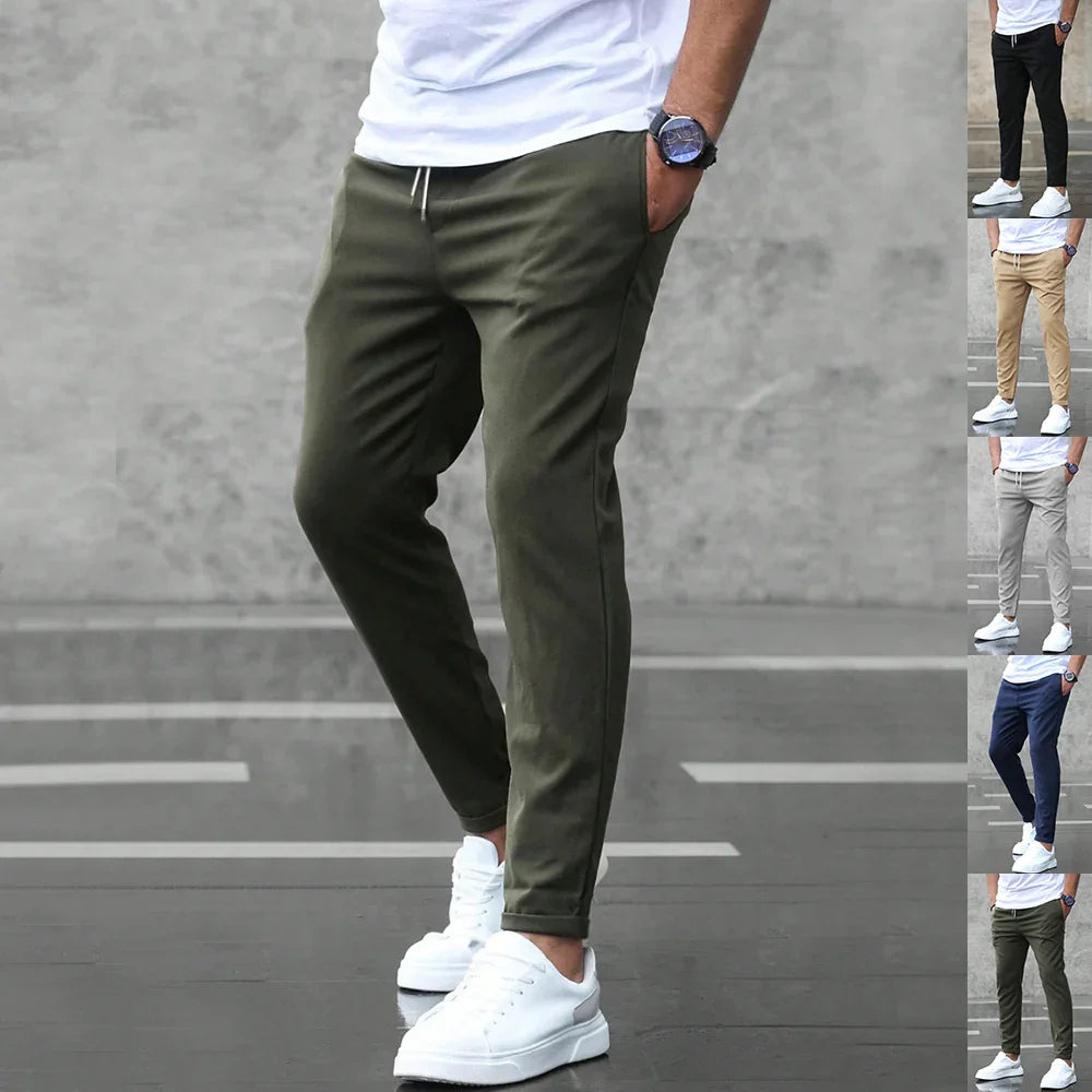 Person wearing olive green pants with a white shirt and white sneakers on a gray background.