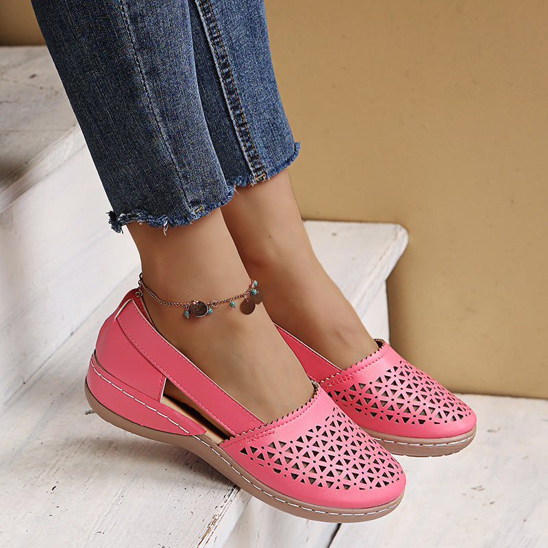 Pink perforated shoes worn with blue jeans on a light wooden floor.