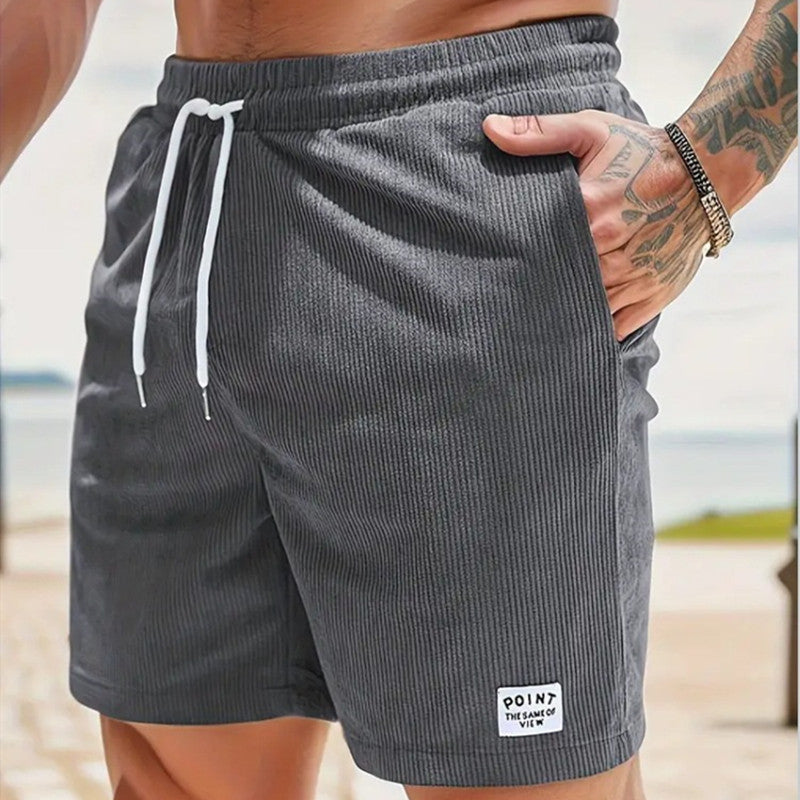 Person wearing gray shorts with a white drawstring, standing on a beach.